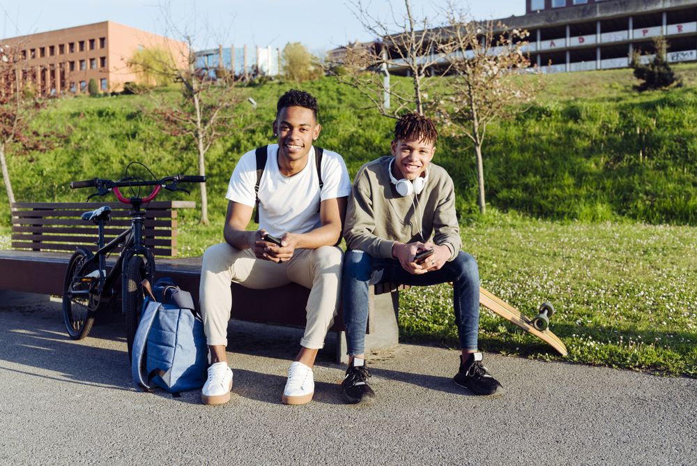 Young Black men sitting on bench with smartphone