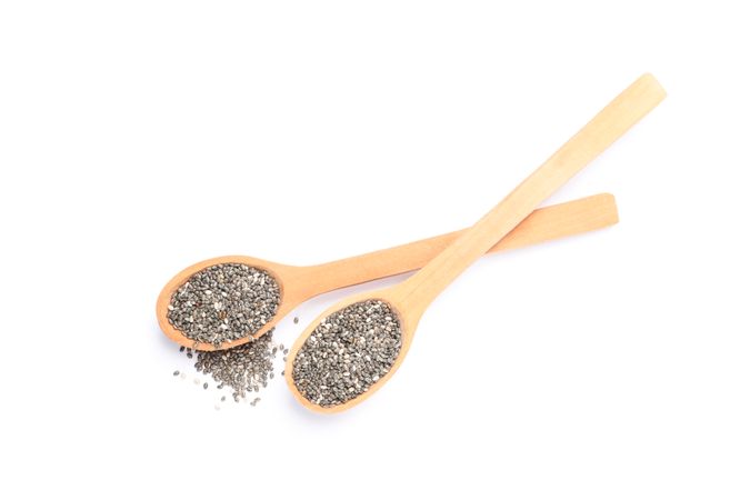 Chia seeds and wooden spoons isolated on plain background