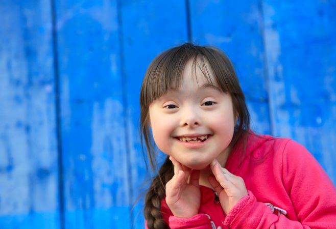 A girl with Down syndrome smiling with her hands on her chin
