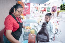 An adult Hispanic woman is preparing a vanilla ice cream for a young woman client in a street market stall