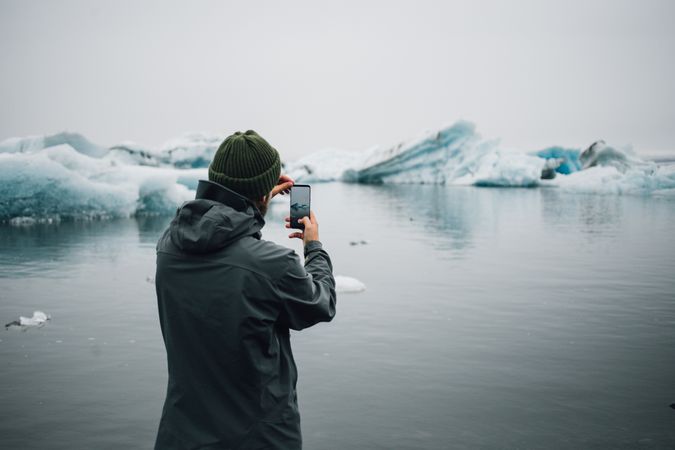 Man taking picture of glacier with smart phone on overcast day