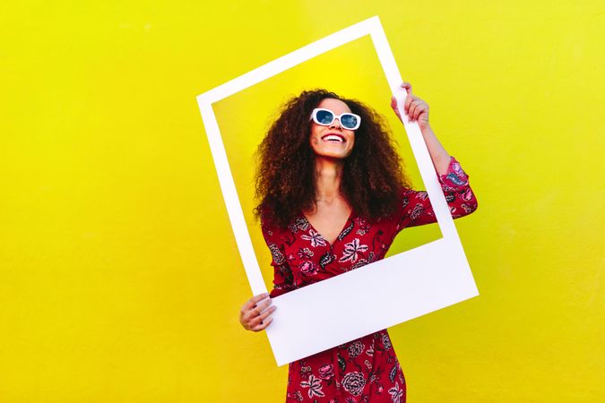 Beautiful female model posing with empty picture frame against yellow wall