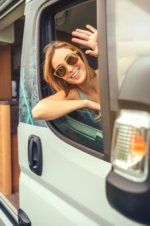 Female passenger in motorhome waving out window, vertical