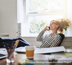 Woman leaning back at her home desk while taking a call 48YeRb