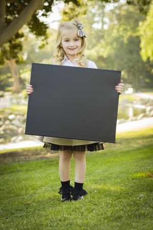 Cute Little Blonde Girl Holding a Chalkboard Outdoors.