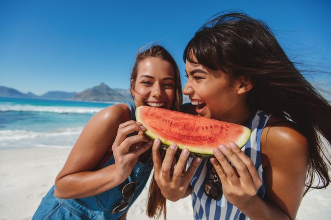 Two female friends sharing watermelon slice on the beach
