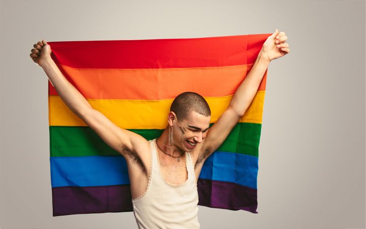 Man smiling with a rainbow flag with “too femme” written on his face