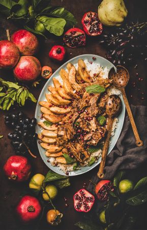 Plate of lamp chops over rice, and quince on table with grapes and pomegranate, vertical composition