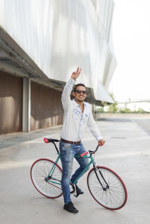 Male sitting on bike next to building with arm up