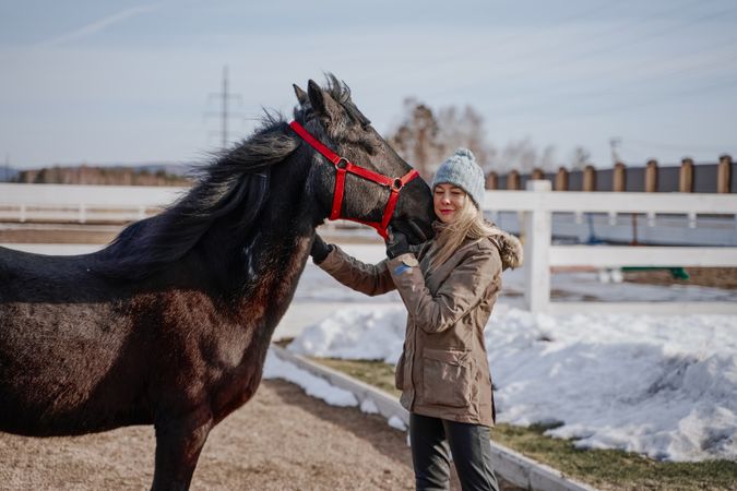 Warm dressed woman with brown horse by hay
