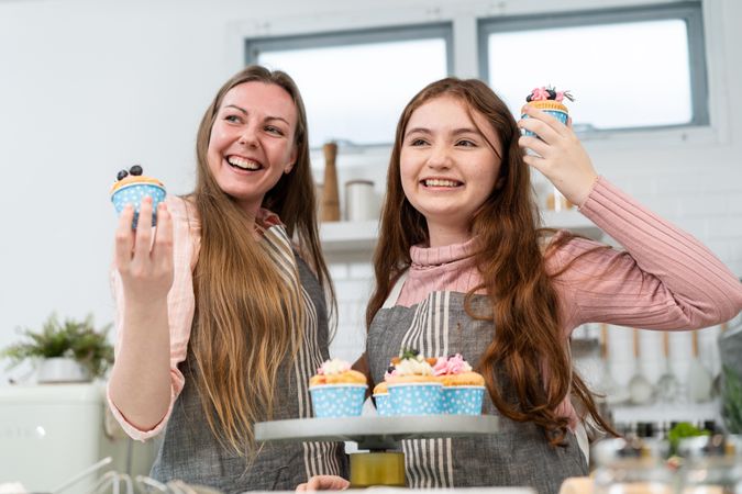 Smiling mother and daughter proud showing homemade cupcakes