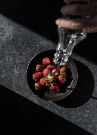 Hand with bottle pouring water on strawberries in plate