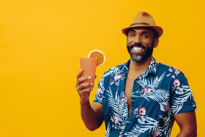 Happy male holding a drink while wearing colorful shirt with yellow background, copy space