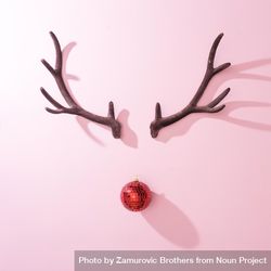 Red Christmas disco ball bauble with reindeer antlers on pink background with shadows 5w3yv5