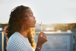 Woman blowing bubbles backlit by sun