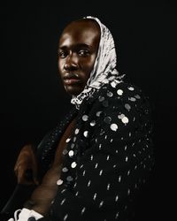 Side view of man in polka dot top and headscarf sitting against dark background