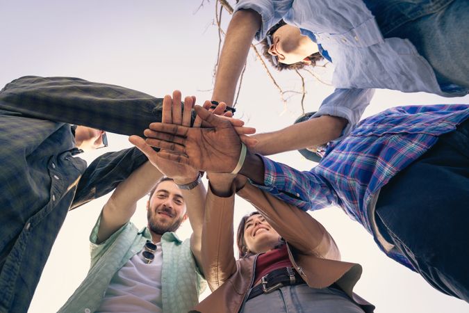 Worm's eye view of a diverse group of happy friends putting their hands together in a huddle.