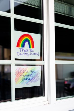 Two handwritten signs with colored rainbows taped on home window thanking essential workers