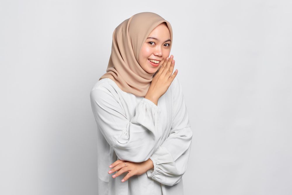 Asian female in headscarf telling secrets behind her hand