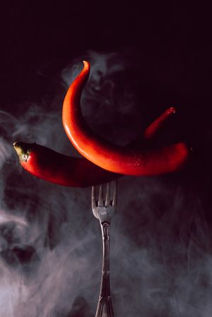 two red chili pepper in fork on a dark background with smoke