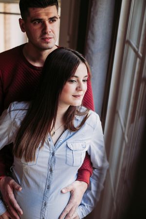 Pregnant woman with husband looking at window at home