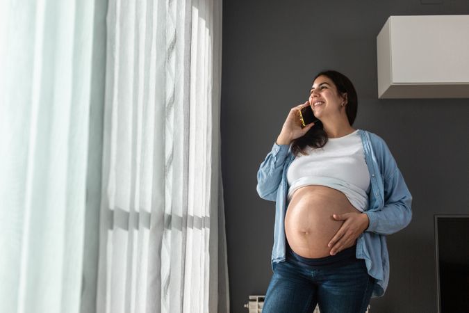 Pregnant woman talking with smartphone at home