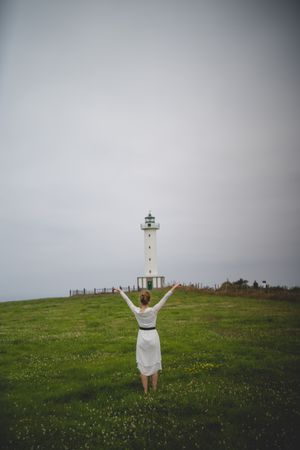 Woman walking in green meadow near lighthouse