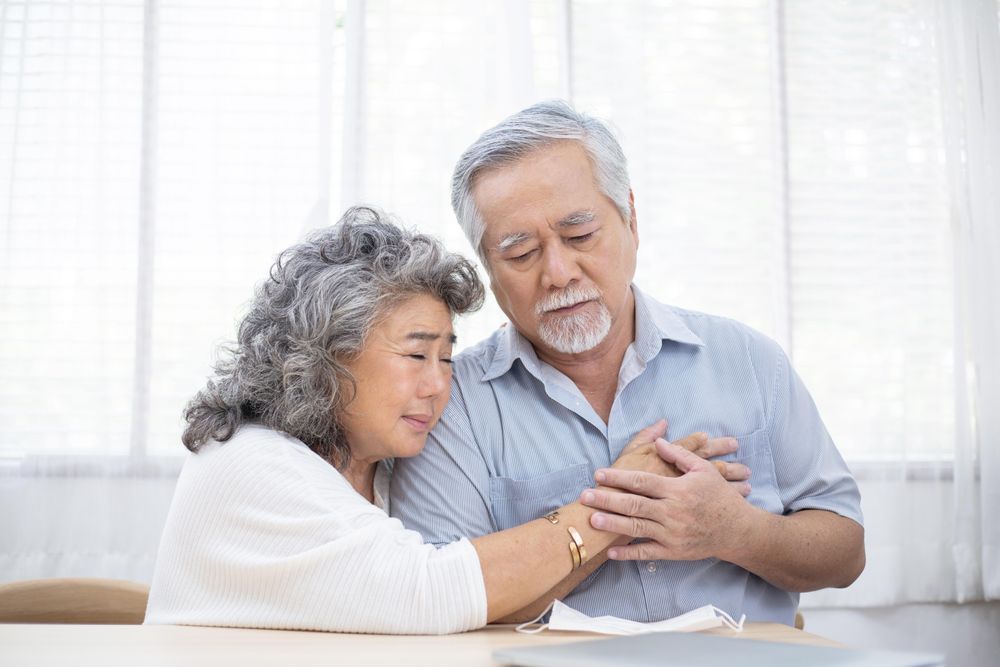 Asian wife embraces mature husband after receiving diagnosis of sickness