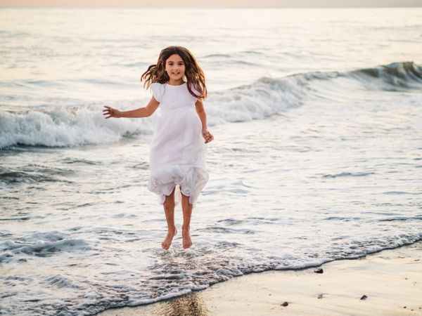 Excited girl running along beach in daylight