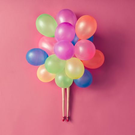 Doll legs with colorful balloons on pastel pink background