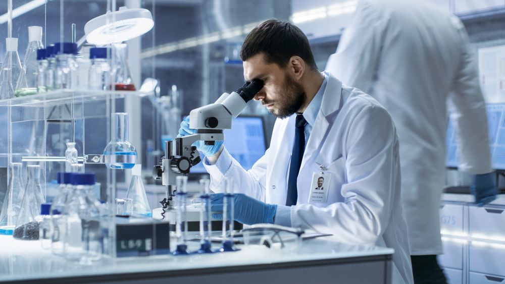 Research Scientist Looks into Microscope in Research Centre.