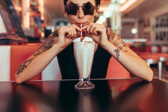 Woman wearing star shaped eyeglasses drinking milkshake at a restaurant