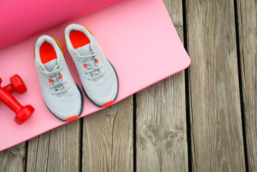 Karemat, sneakers and dumbbells on wooden background, space for text