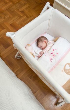 Baby girl sleeping in a cot with pink trimming with pacifier and toy