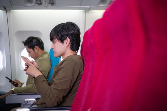 Asian boy using mobile phone seated in an airplane