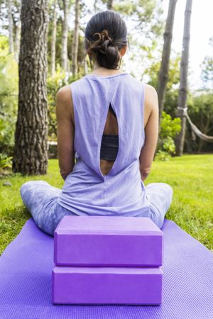 Back view of a woman in sportswear sitting on her yoga mat. Vertical shot
