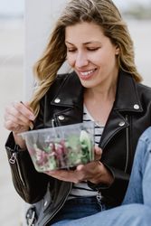 Content woman eating salad from plastic bowl sitting on wooden terrace