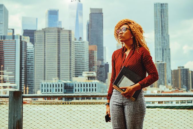 Professional Black female holding her notebooks in front of Manhattan and the Hudson River