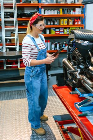 Mechanic with security glasses and digital tablet review motorcycle documentation on garage
