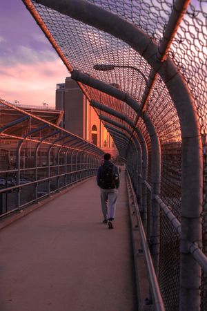 Man in dark jacket and jeans walking on bridge