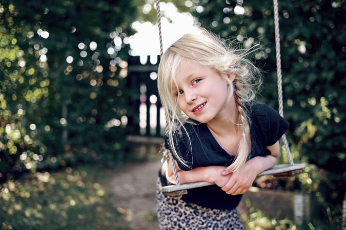 Blonde girl with braided hair playing on outdoor swing
