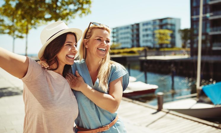 Two women laughing together and holding each other on sunny day next to the river
