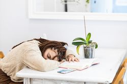 Woman asleep on a book while sitting at a table