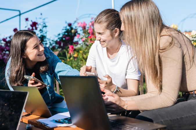 College woman taking a break from studying showing messages on phones while talking and laughing.