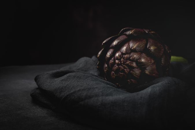 Fresh raw purple artichokes on dark background.