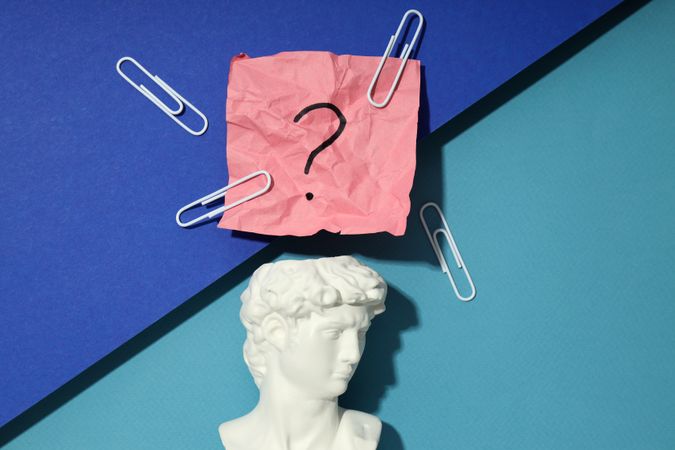 Marble bust of David with crumpled pink post it note with question mark and paper clips, closeup