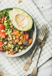 Healthy vegan lunch bowl with avocado, sprouted grains, vegetables, with forks on checkered napkin