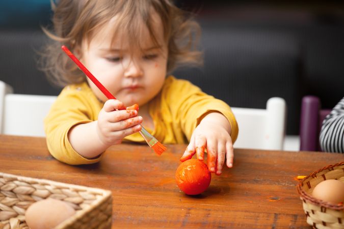 Toddler girl painting egg at table