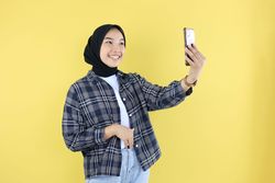 Cheerful Young Asian Muslim Woman in Checkered Blue Shirt and Hijab doing Selfie