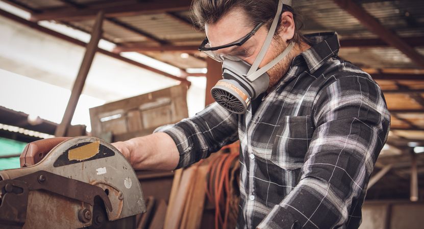 Male carpenter using electric saw cutting wood board in workshop